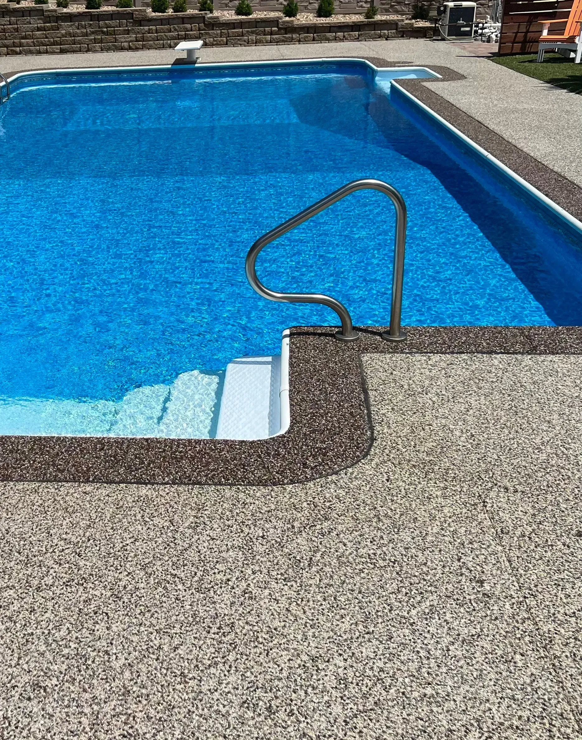A blue backyard swimming pool featuring white entry steps, a chrome handrail, and a textured stone-look pool deck.