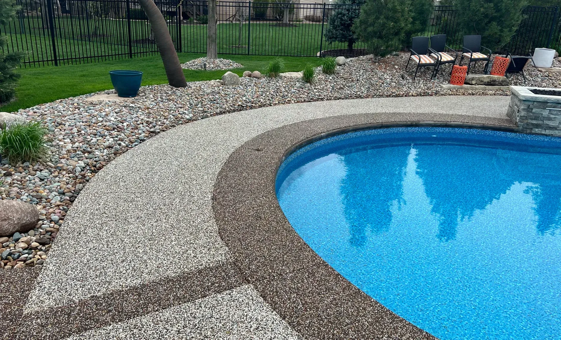 A swimming pool with blue water surrounded by a multi-textured stone patio and a decorative rock landscape garden.