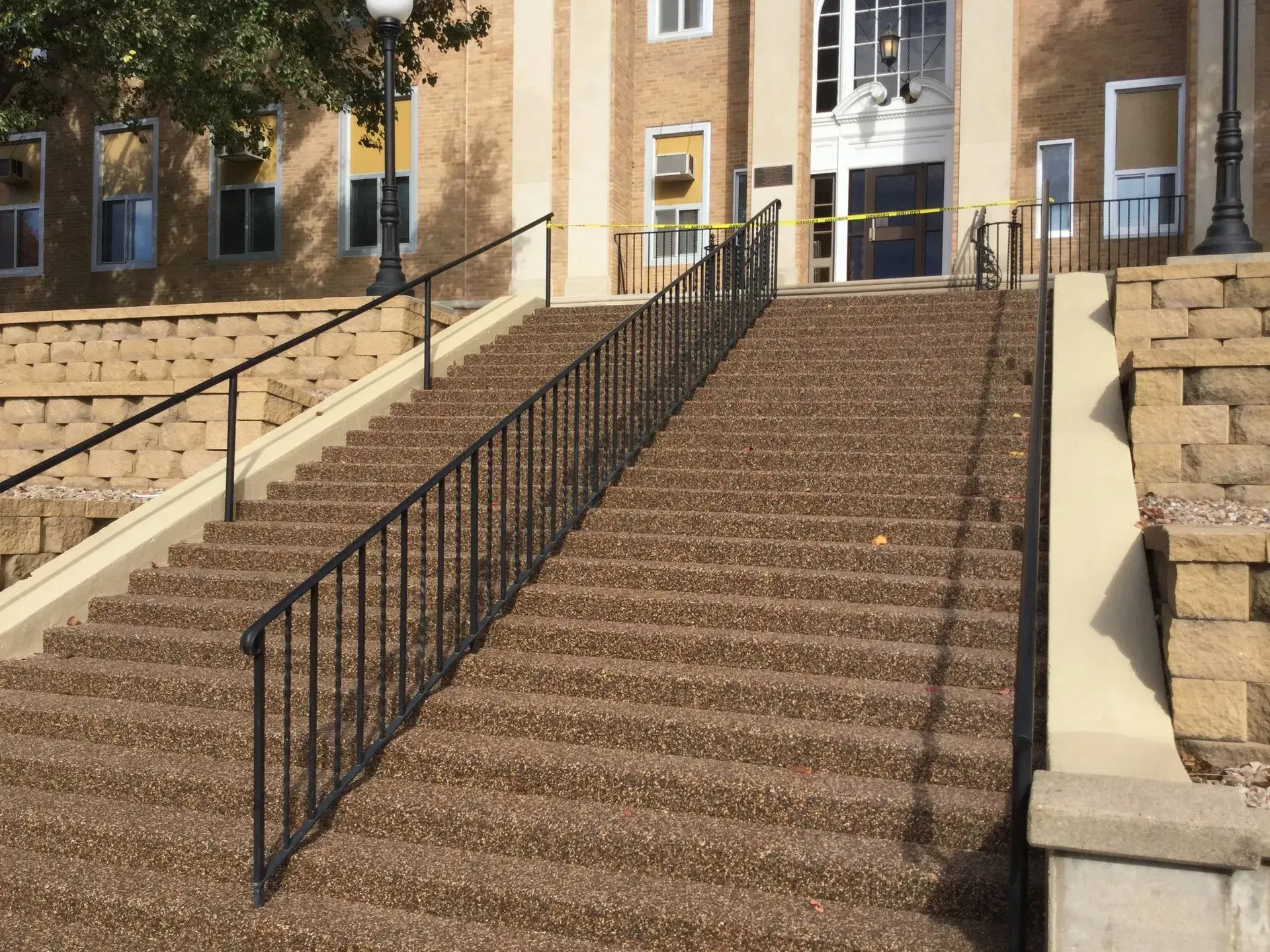 A wide, multi-step outdoor concrete staircase with black metal railings leading to the entrance of a brick building.
