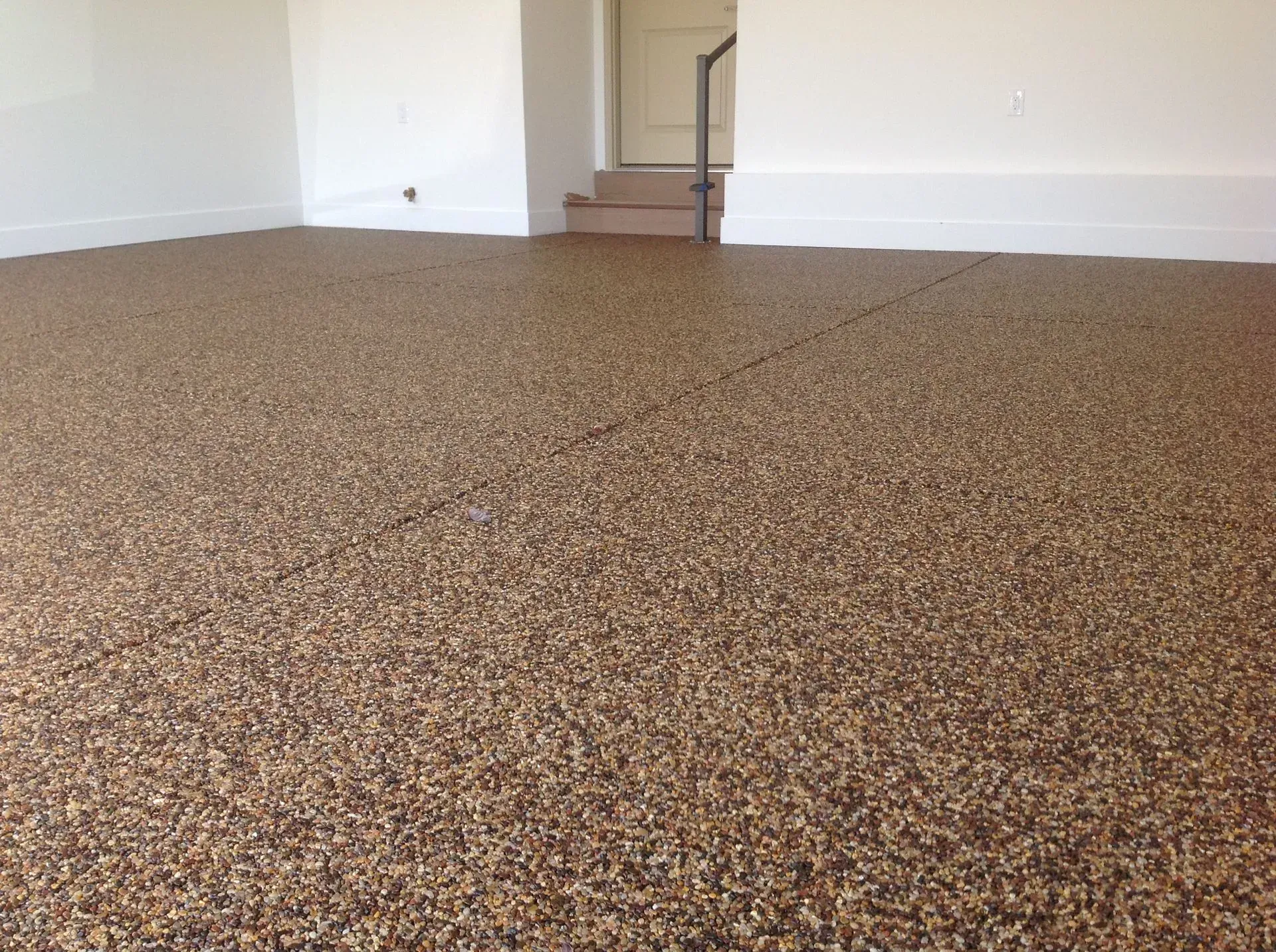 An indoor space with a speckled brown epoxy floor, white walls, and a small set of stairs leading to a doorway.