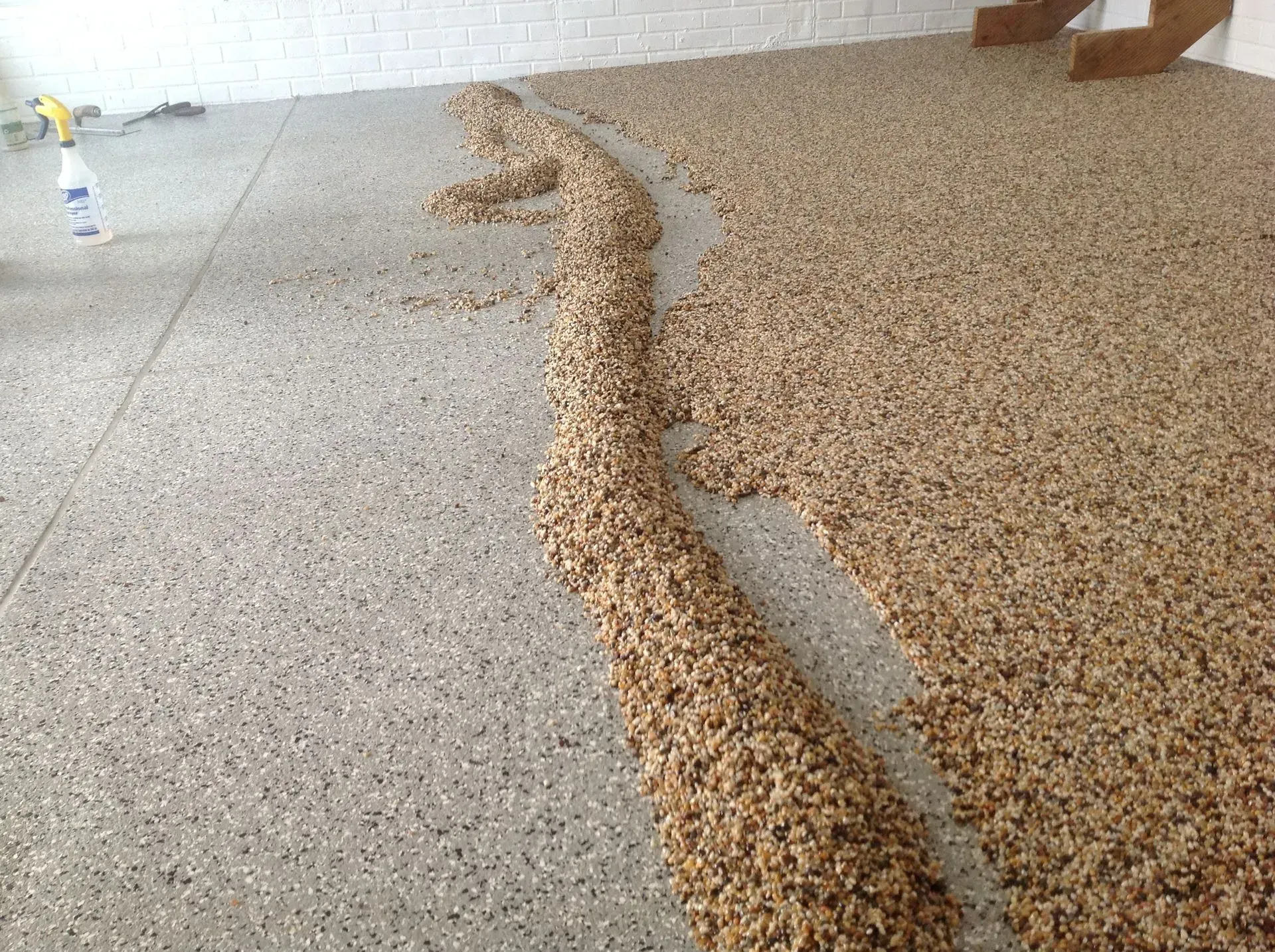 A garage floor with a smooth, light gray flake finish on the left and a thick, textured tan aggregate finish on the right.