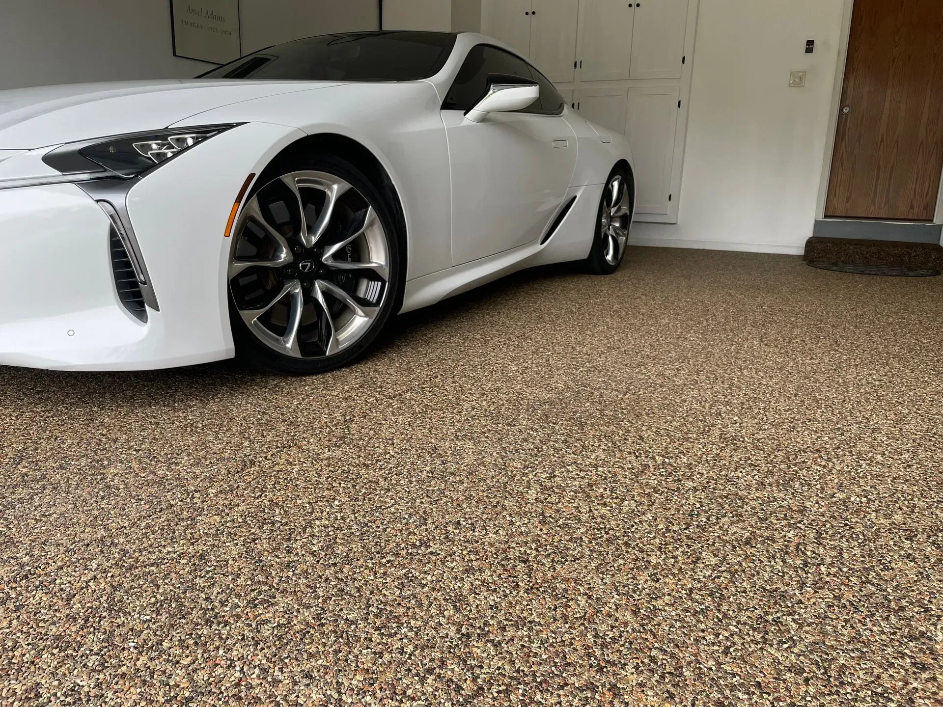 A white Lexus luxury coupe parked in a garage with a decorative, multi-colored speckled epoxy floor.