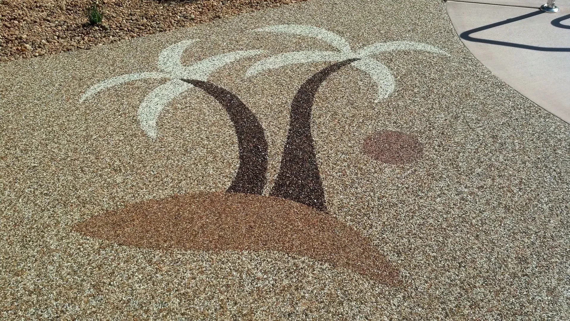 A decorative pebble mosaic in a ground surface depicting two palm trees on a small island.