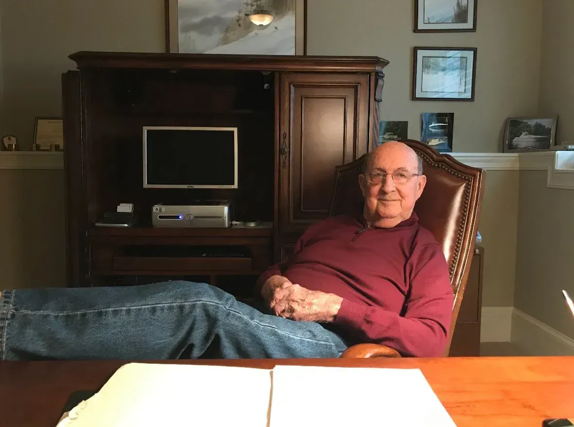 An individual wearing a burgundy long-sleeved shirt and blue jeans sits in a brown leather office chair.