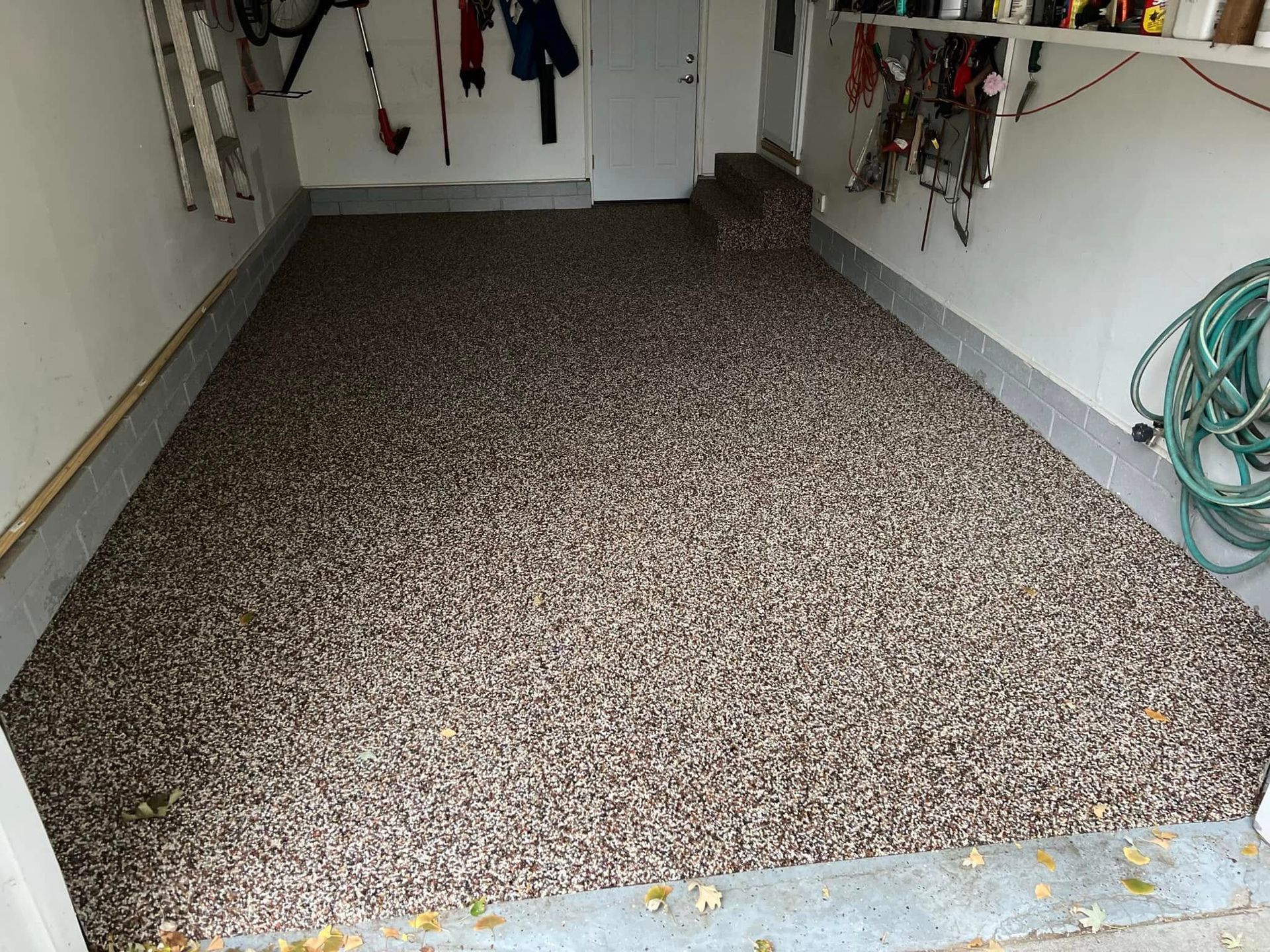A garage floor covered in brown, gray, and white speckled epoxy coating, with items hanging on the walls