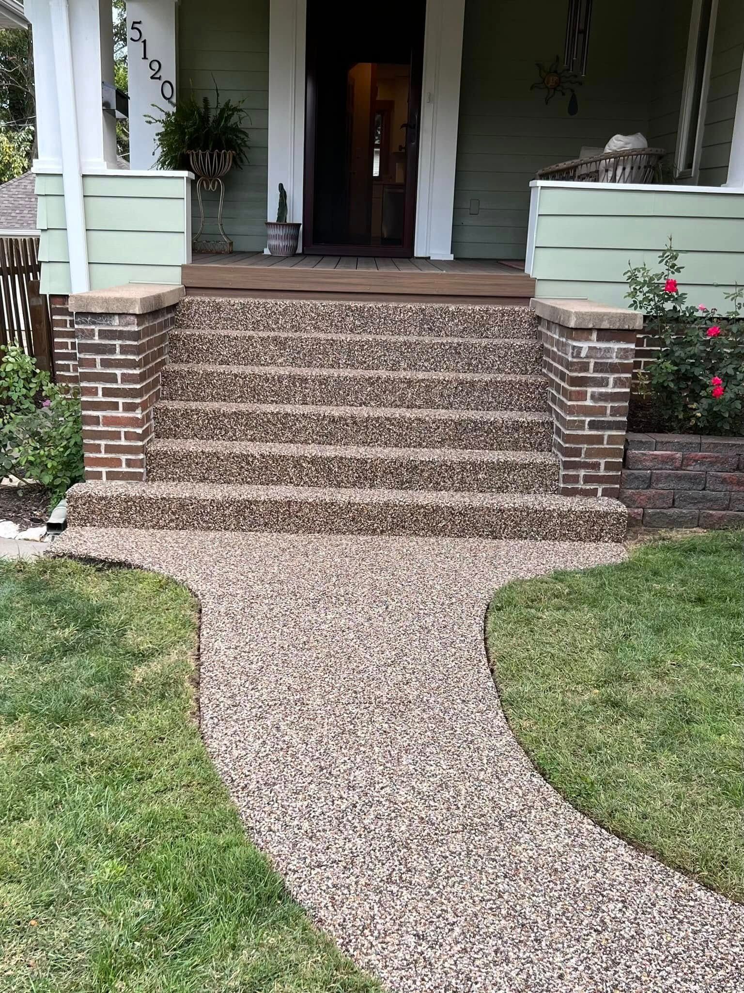 A front walkway made of aggregate leads to five steps with brick pillars leading up to a house porch