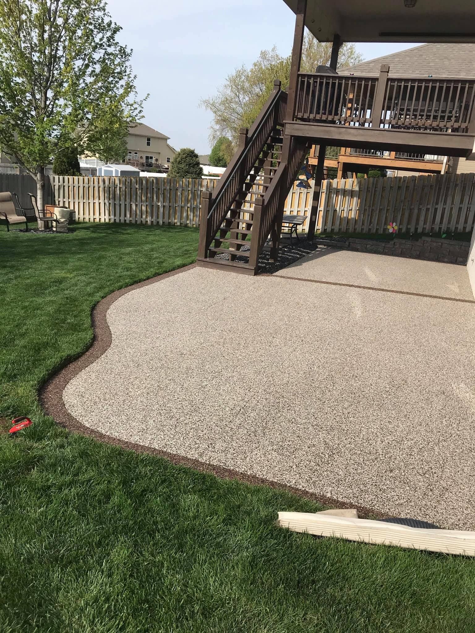 A gravel patio area bordered by a plastic edging strip sits under a wooden deck in a residential backyard