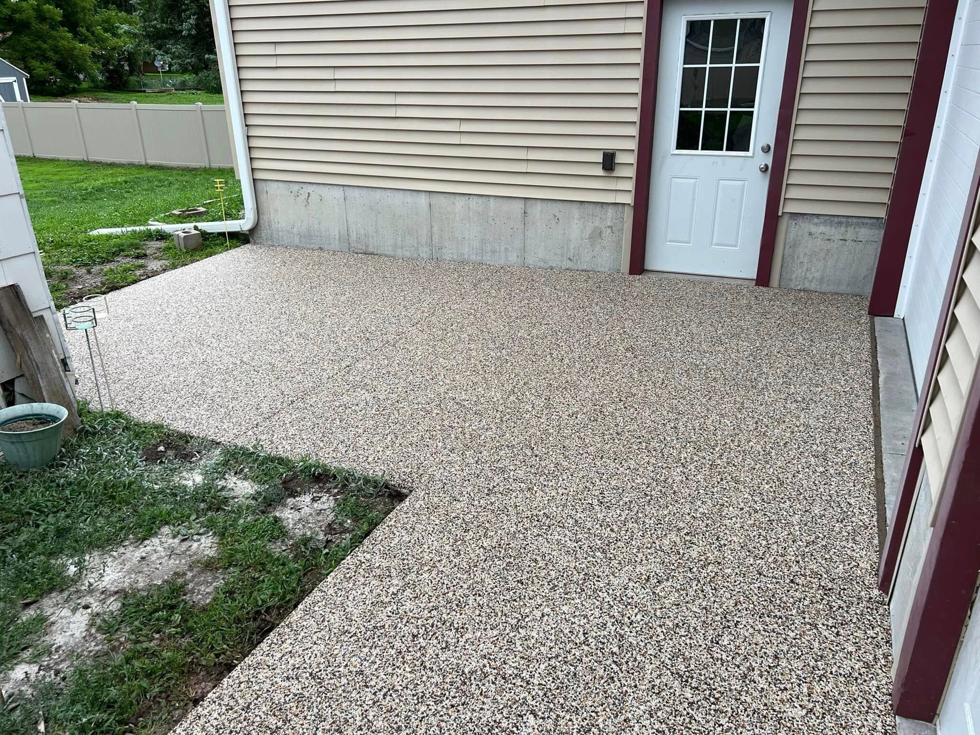 A light-colored stone patio sits beside a building with beige horizontal siding and a white door