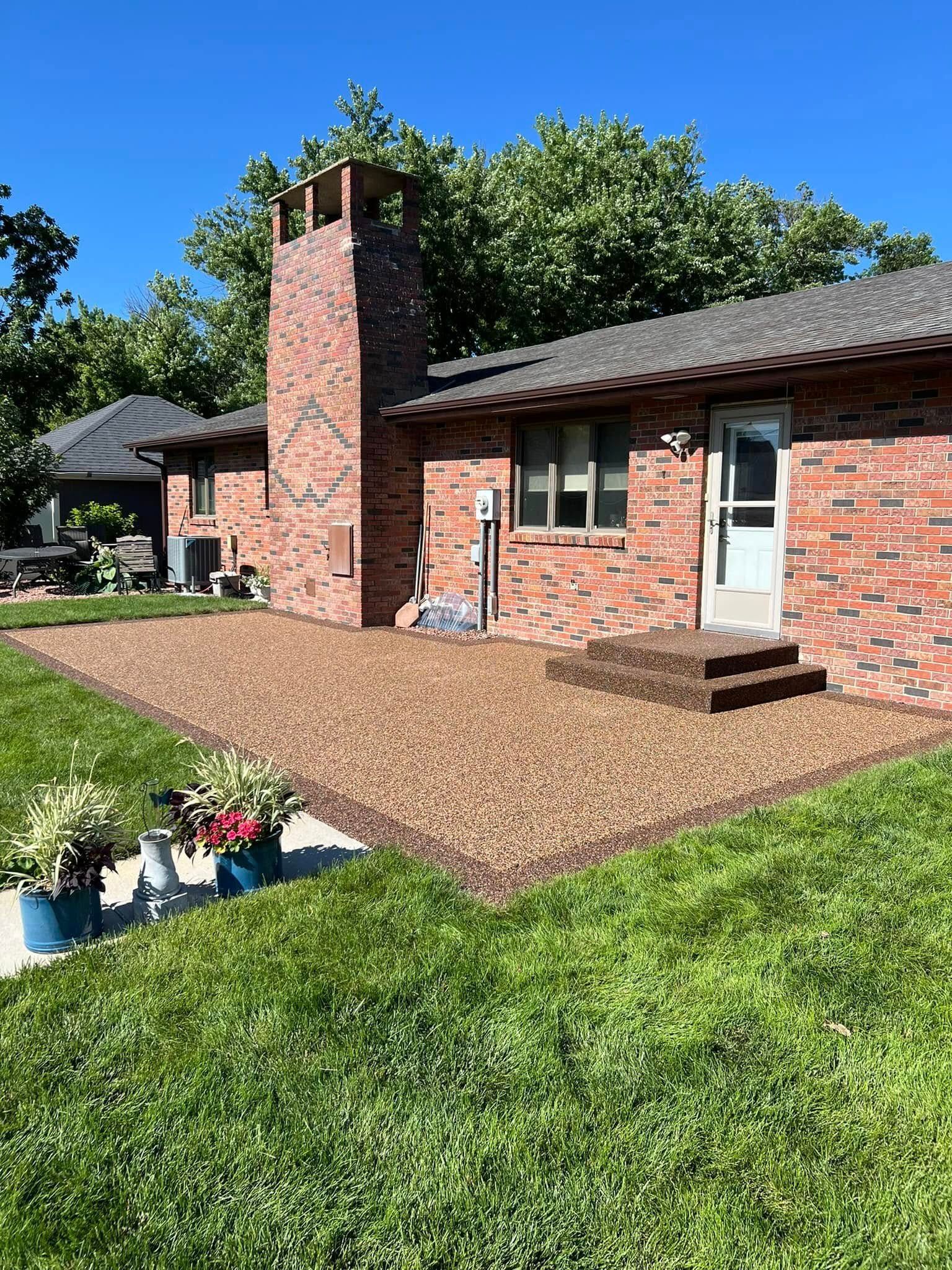A red brick house with a large gravel patio, a chimney, and a white screen door, set against a bright blue sky