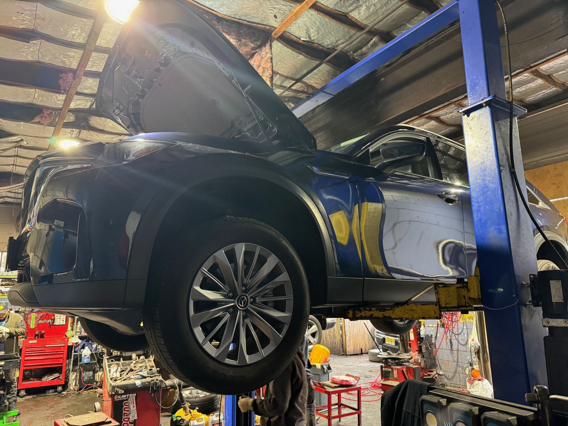 Dark blue SUV raised on a lift in a garage with hood open, showing the undercarriage.