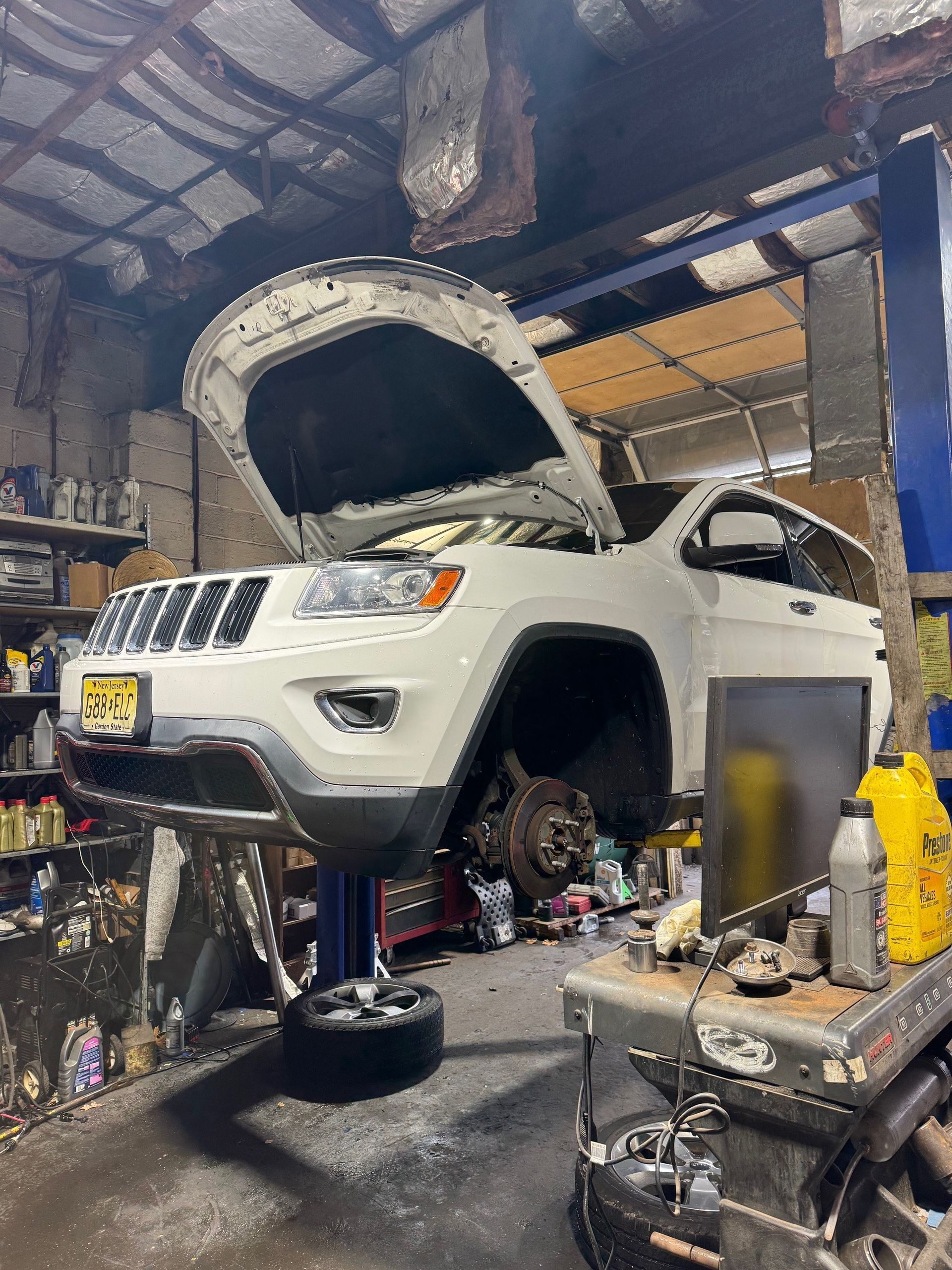 White Jeep Grand Cherokee raised in a garage, hood open for repairs.