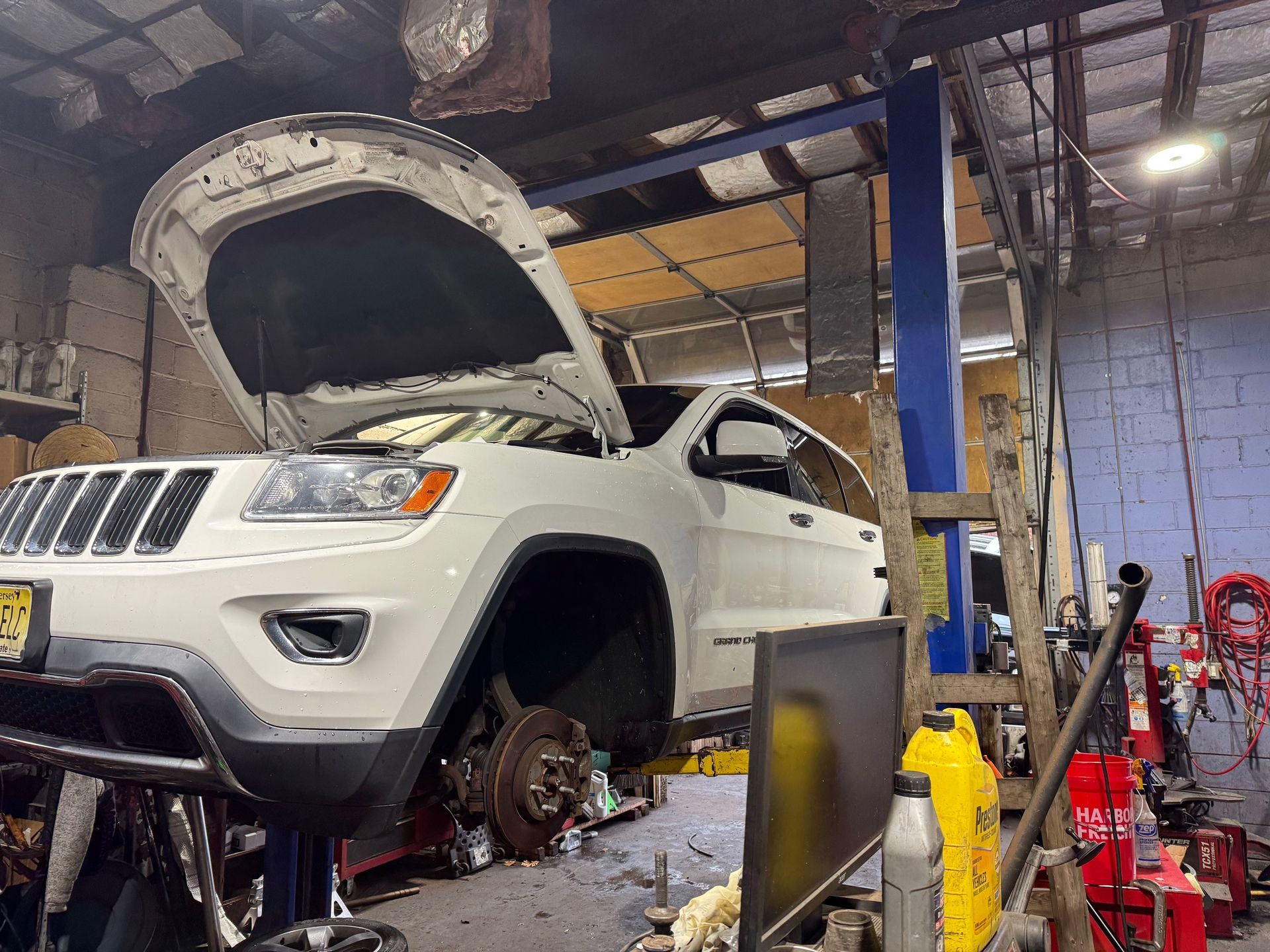 White Jeep Grand Cherokee raised on a lift in a repair shop with its hood open and wheels removed.