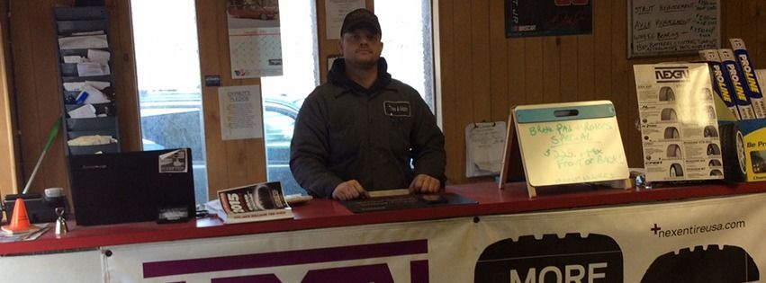 Man in a dark jacket stands behind a red counter in a business setting, a calendar and papers are visible.