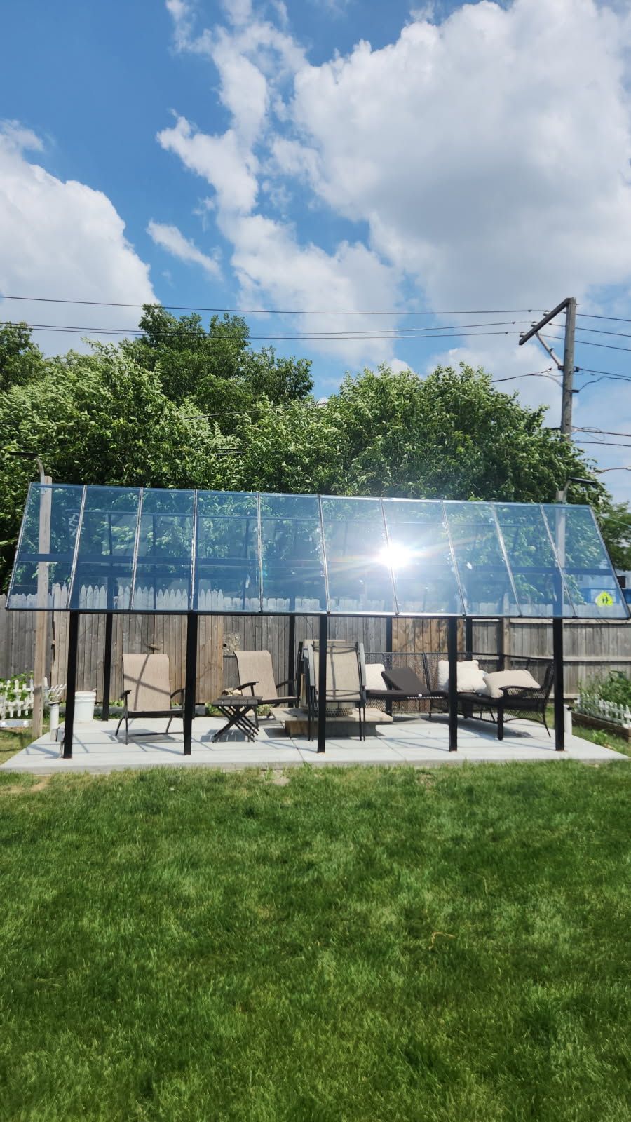 A patio with chairs and a table under a clear roof in a backyard.