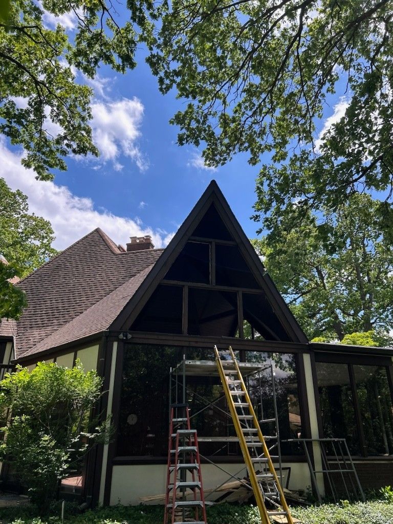 A house with a ladder in front of it and trees in the background.