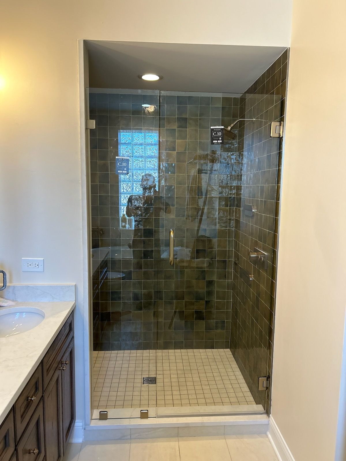 A glass-enclosed shower with tiled walls and floor next to a bathroom vanity with a white countertop.