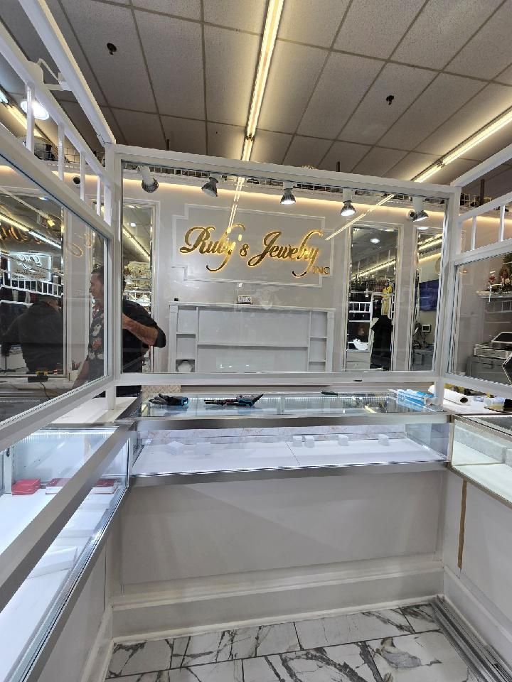 The interior of a bright jewelry kiosk with white marble flooring, display cases, and gold signage reading 