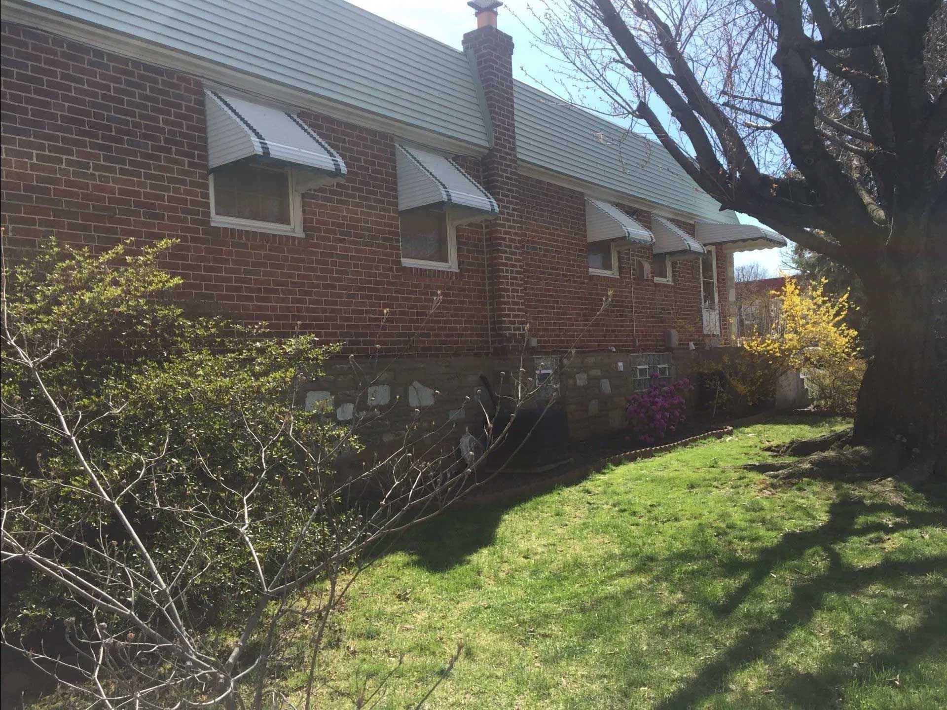 A brick house with white awnings on the windows and a tree in front of it.