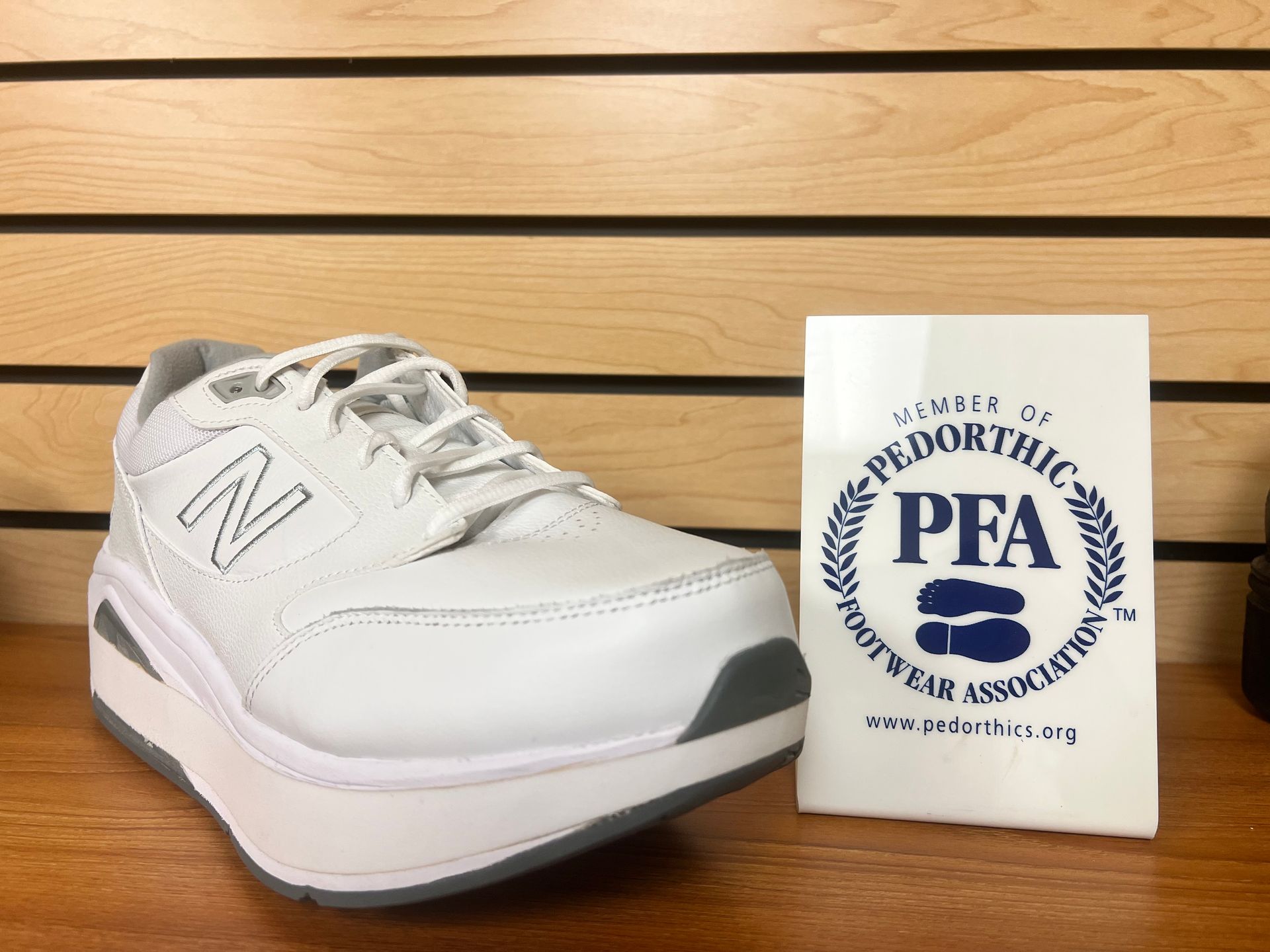 A pair of white shoes is sitting on a wooden shelf next to a pfa t-shirt.