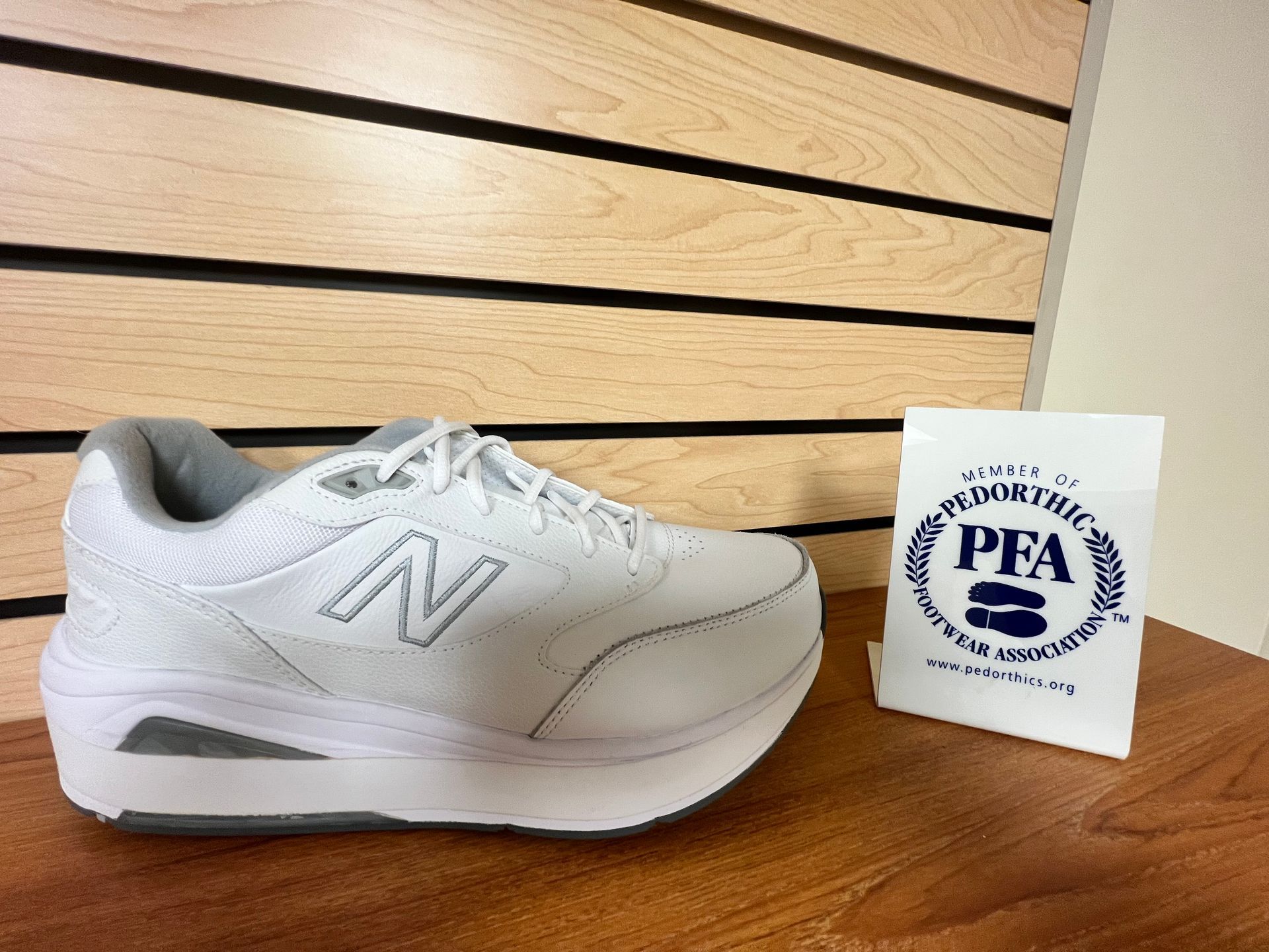 A pair of white new balance shoes are sitting on a wooden table next to a pfa sign.