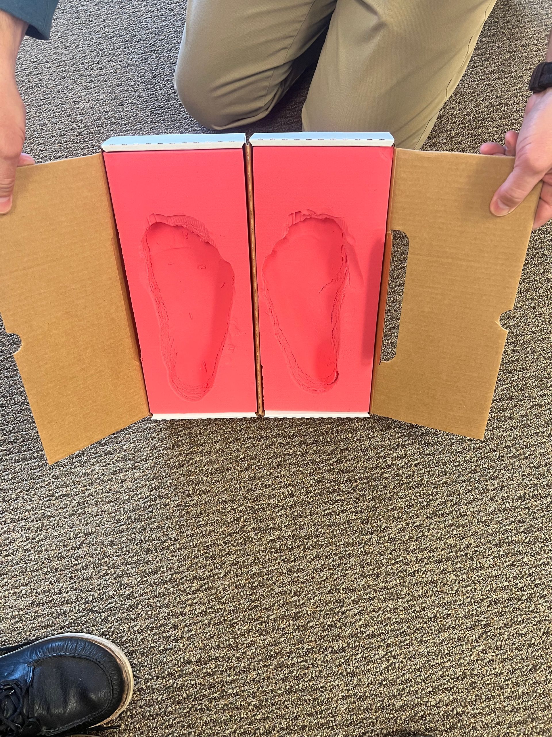 A person is holding a cardboard box with two footprints on it.