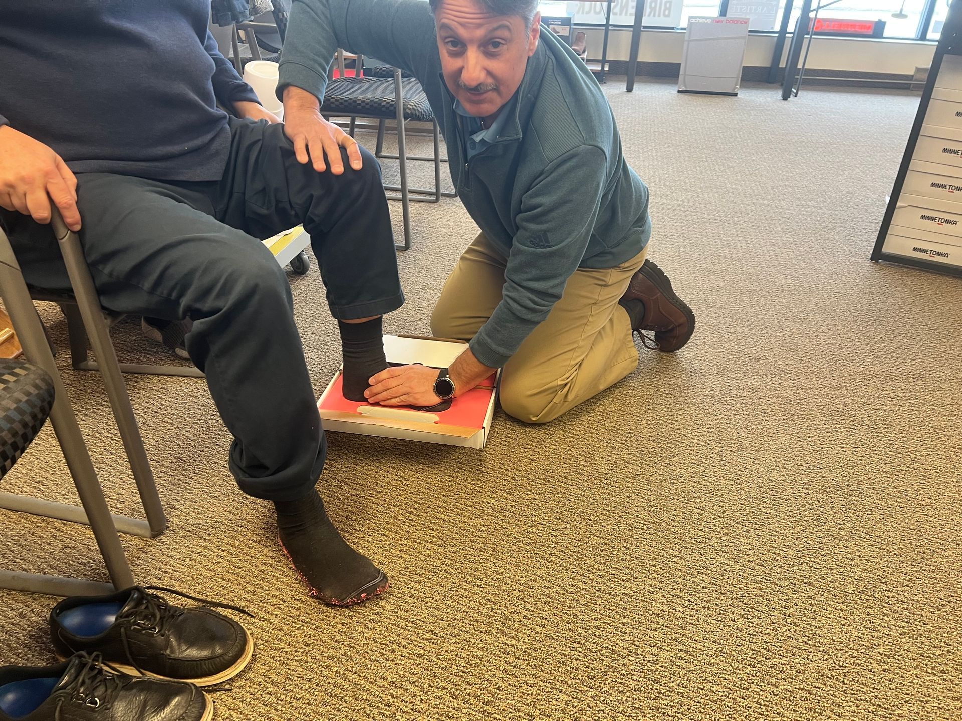 A man is kneeling down to measure a person 's foot in a shoe store.