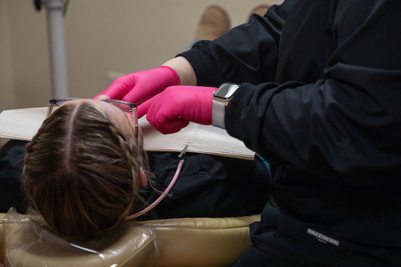 A dental professional wearing bright pink gloves examines a patient lying in a dental chair.