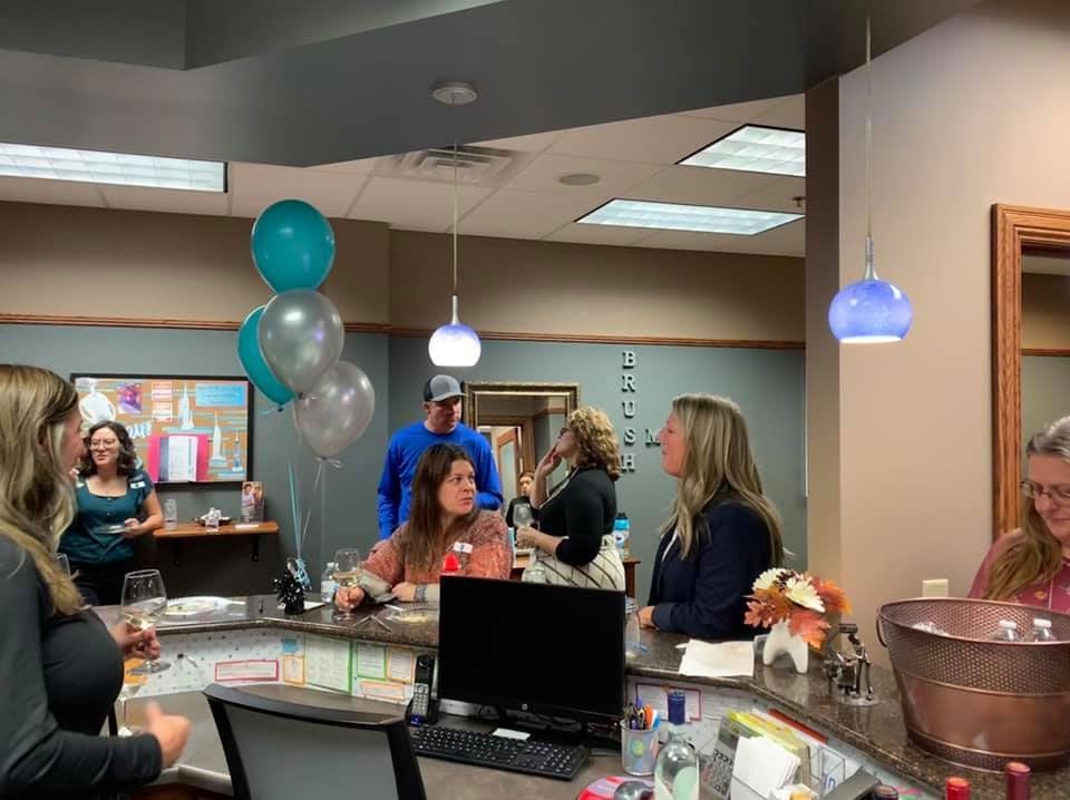 A group of people chat in a brightly lit office space decorated with silver and teal balloons.