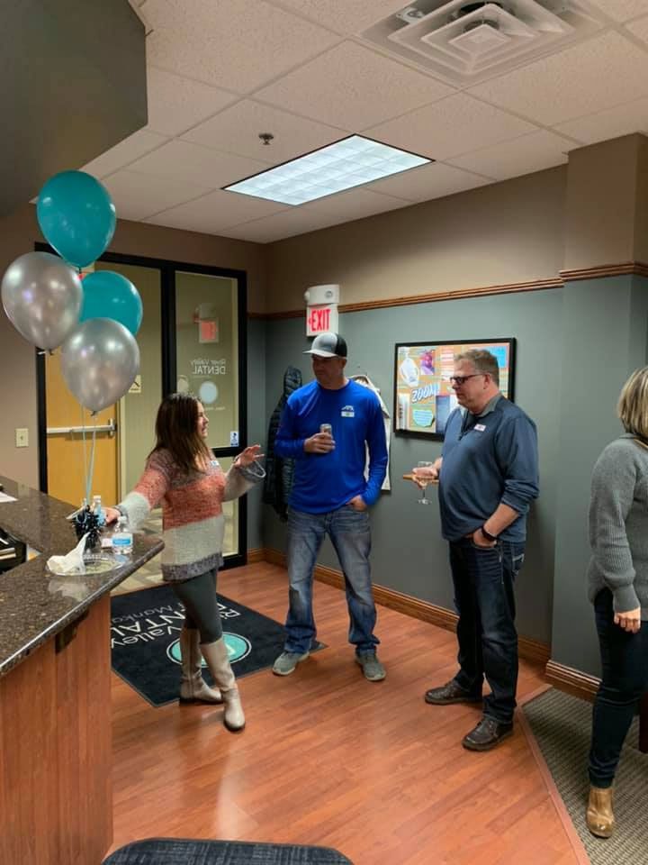 Three people stand in an office lobby decorated with blue and silver balloons, two of them in conversation.