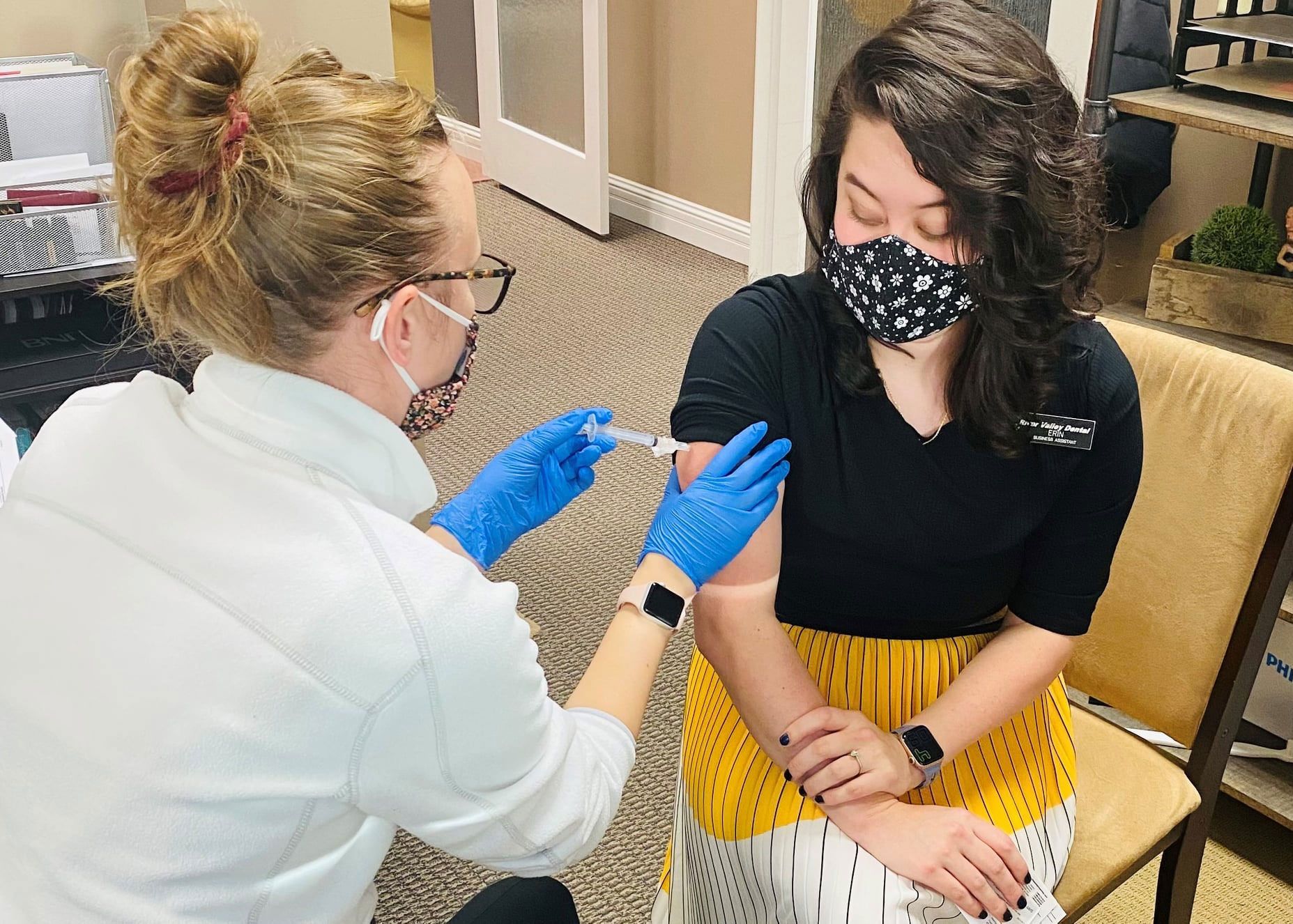 A healthcare worker in a white top and blue gloves administers an injection into a person's upper arm.