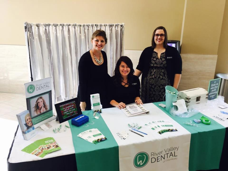 Three people smile behind a table promoting River Valley Dental, complete with branded materials and brochures.