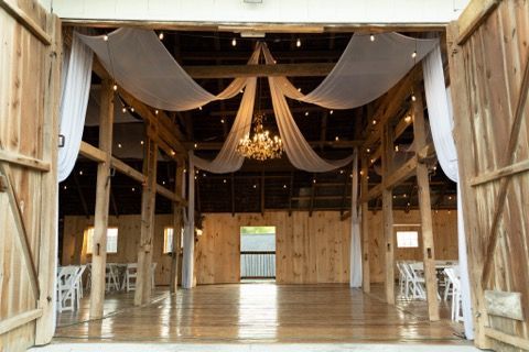 The inside of a barn with white curtains and a chandelier hanging from the ceiling.