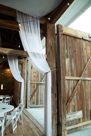 A barn with tables and chairs and white curtains hanging from the ceiling.