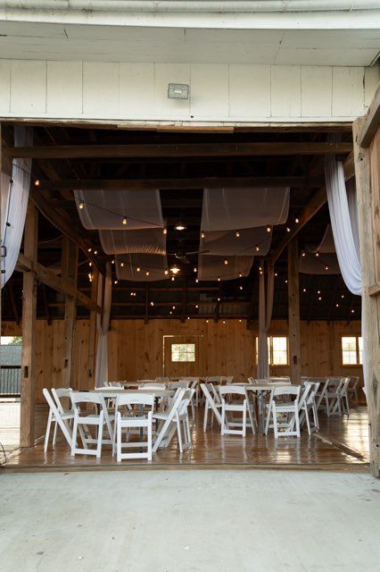 The inside of a barn with tables and chairs set up for a wedding reception.