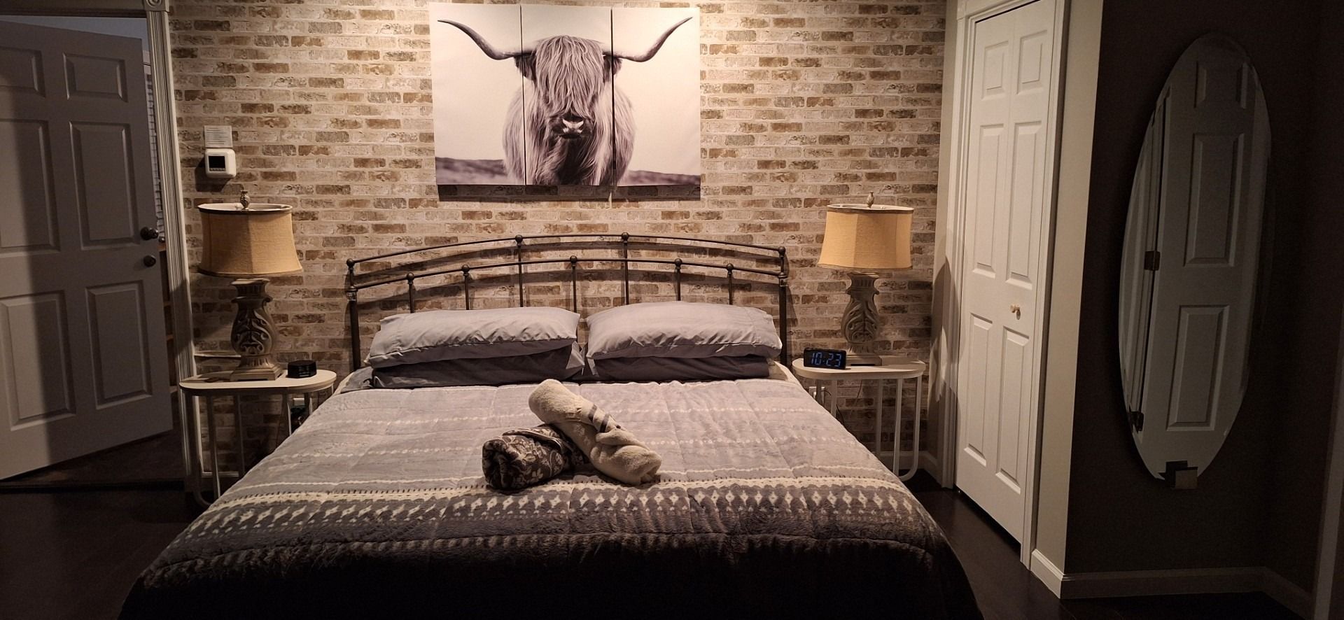 Cozy rustic bedroom with brick walls, cow artwork, and a large bed centered between matching lamps.