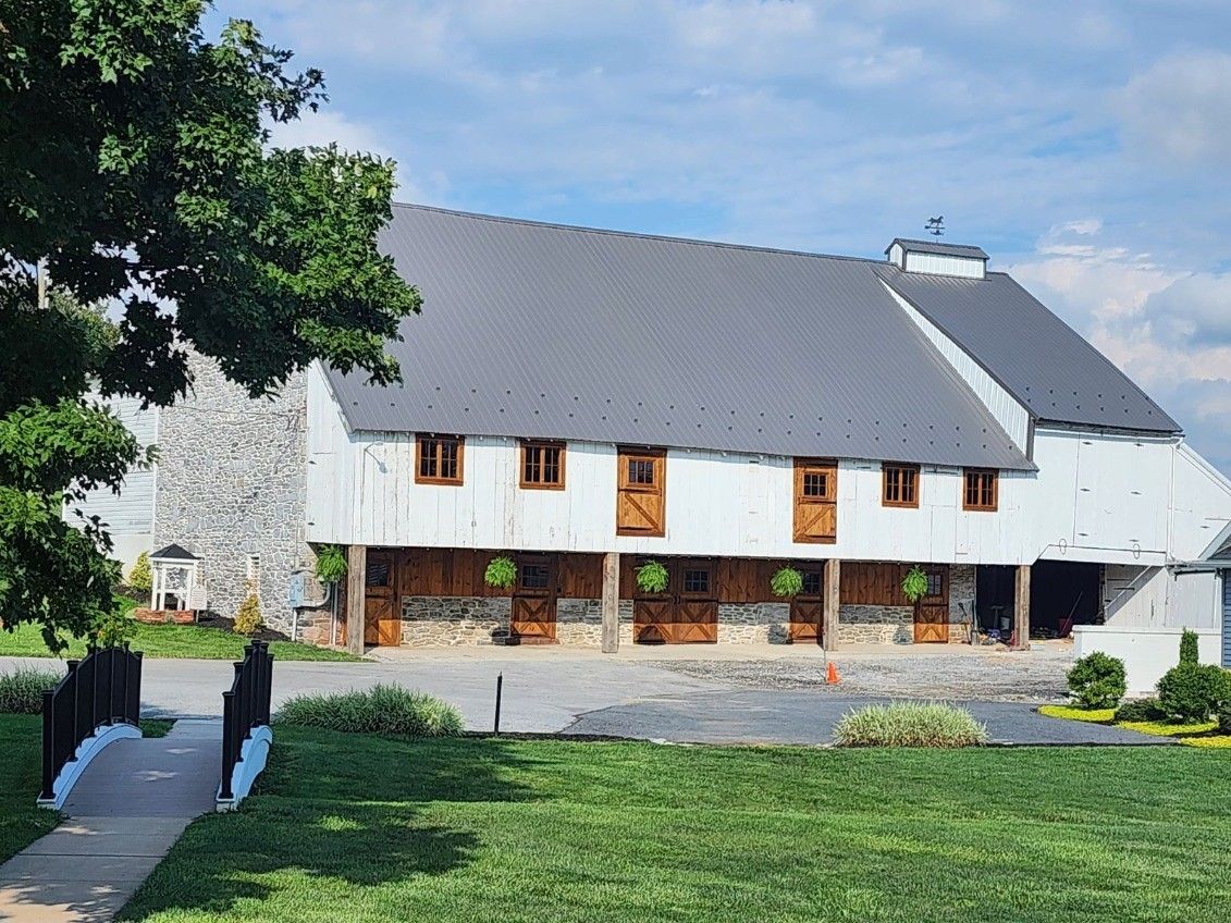White farmhouse with dark roof and flower boxes, set beside a grassy lawn under a blue sky.