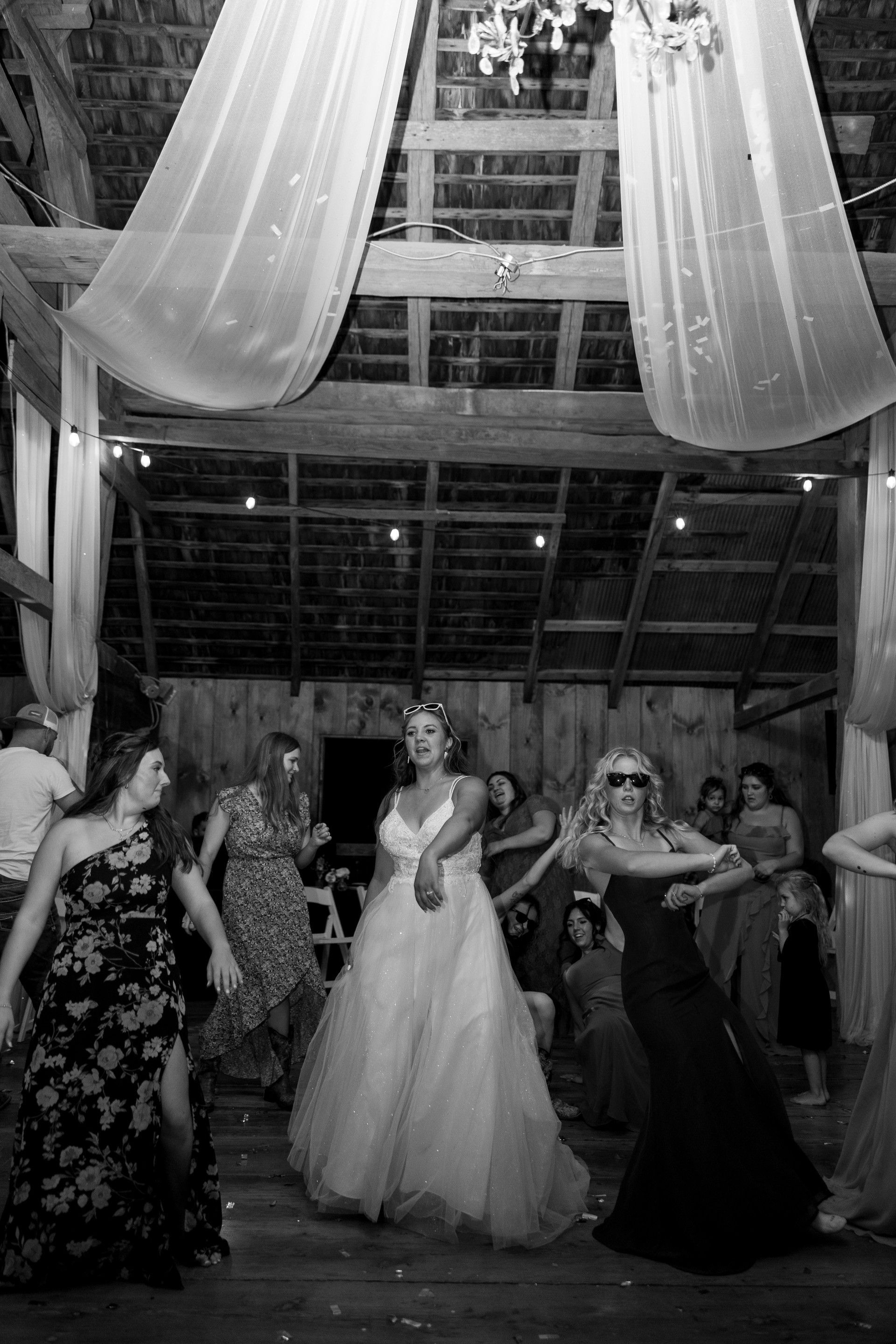 Women dancing at a wedding reception in a barn decorated with draped fabric.
