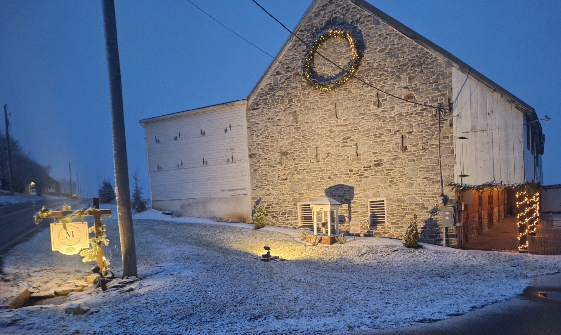 Snowy stone building at dusk with a round clock and warm lights glowing along the side