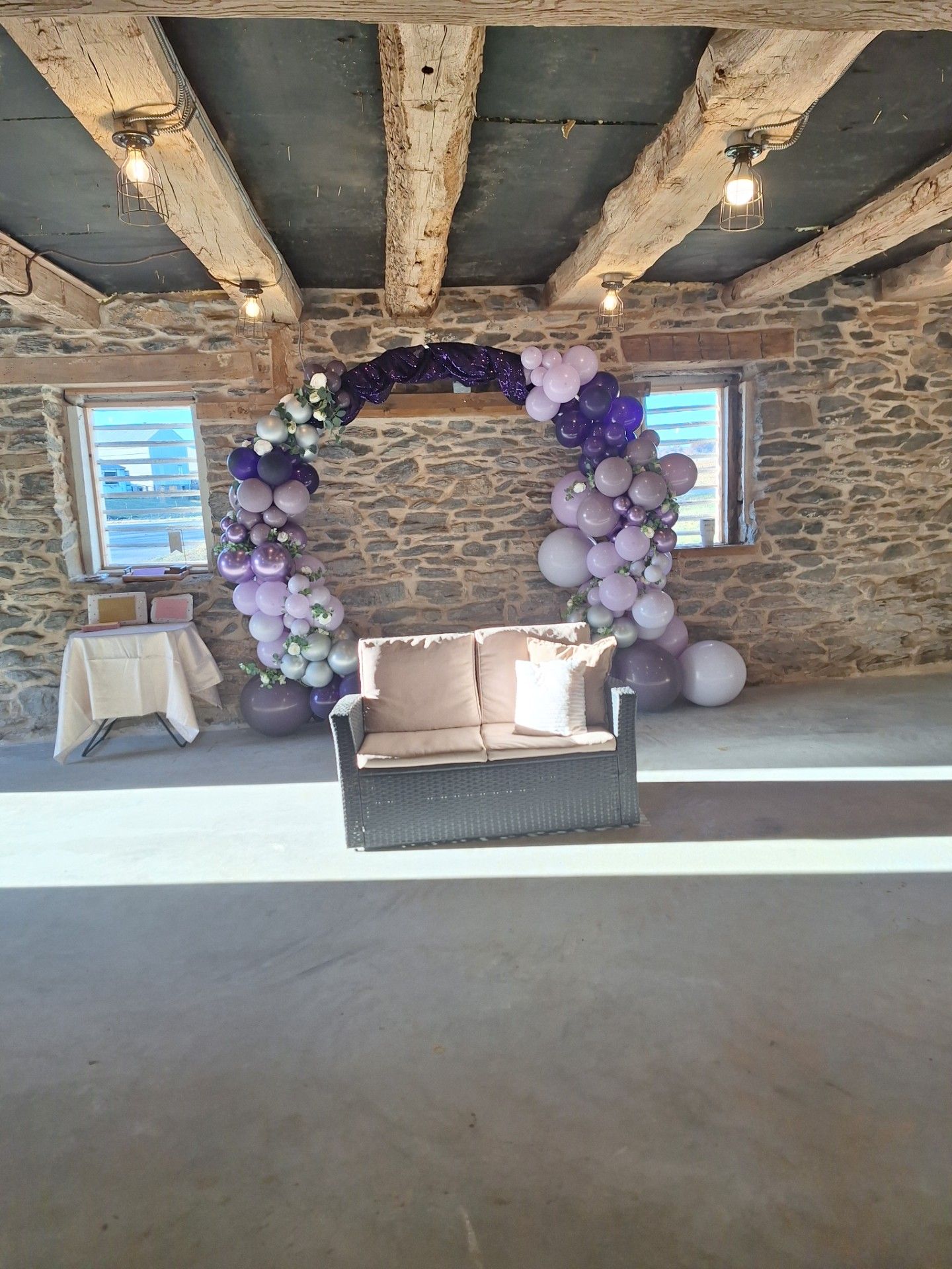 Stone-walled room with purple balloon arch and beige loveseat, decorated for an event.
