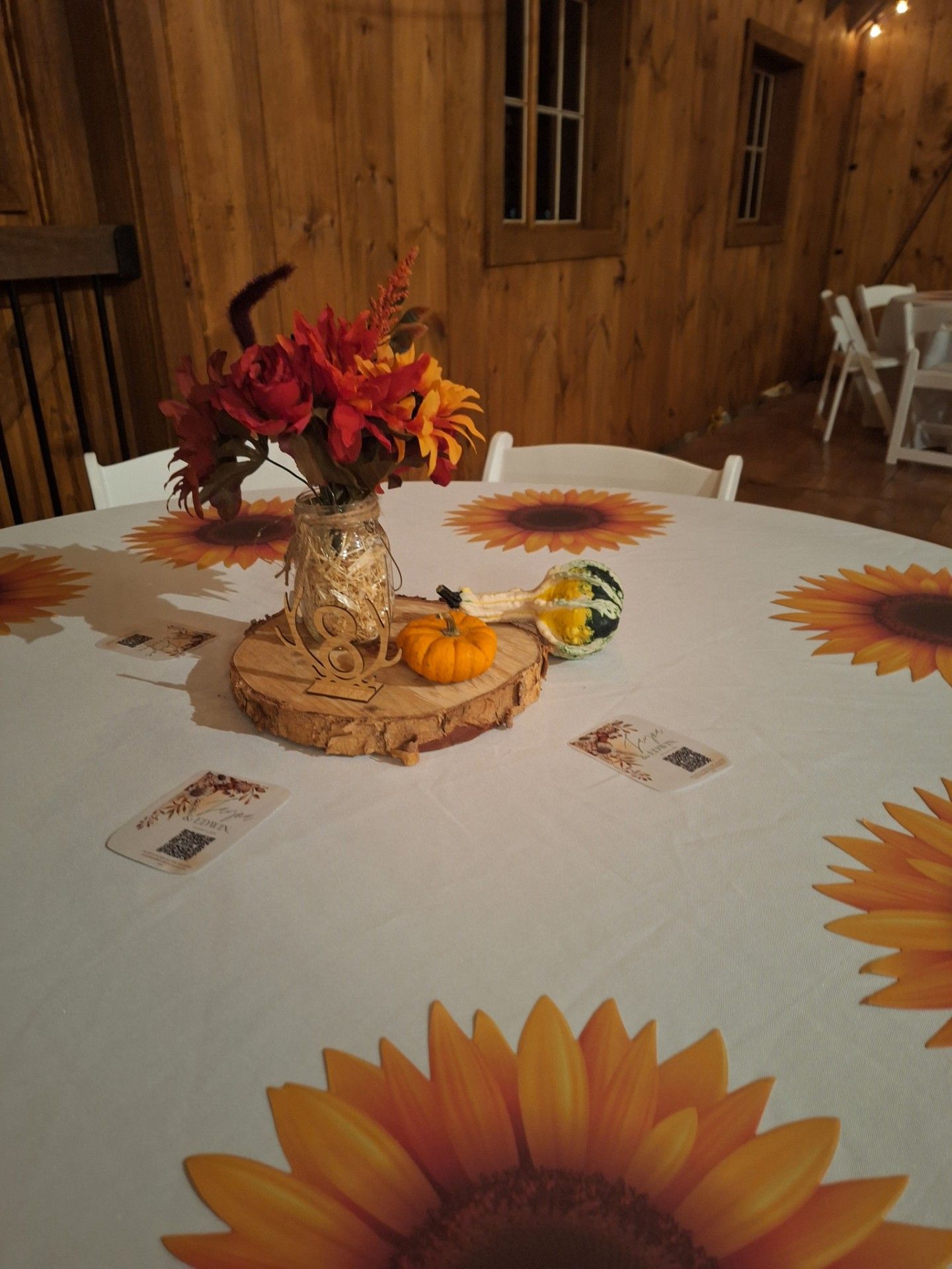 Fall table with sunflower tablecloth, flower centerpiece, and small pumpkins in a rustic wooden room