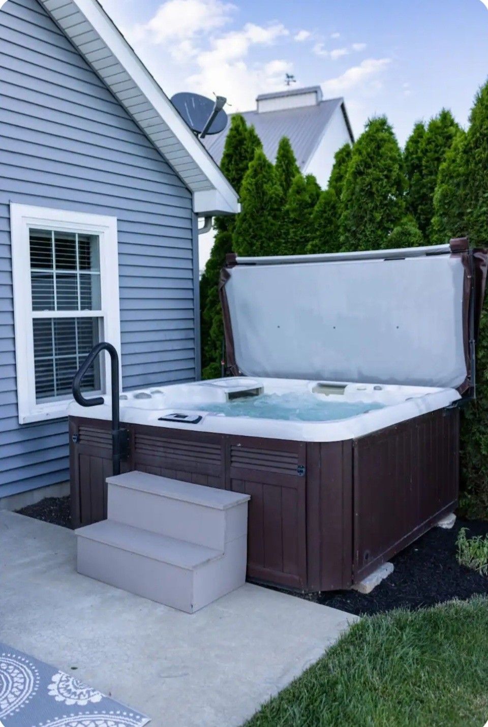 Backyard hot tub beside a house, with steps and privacy hedge fencing
