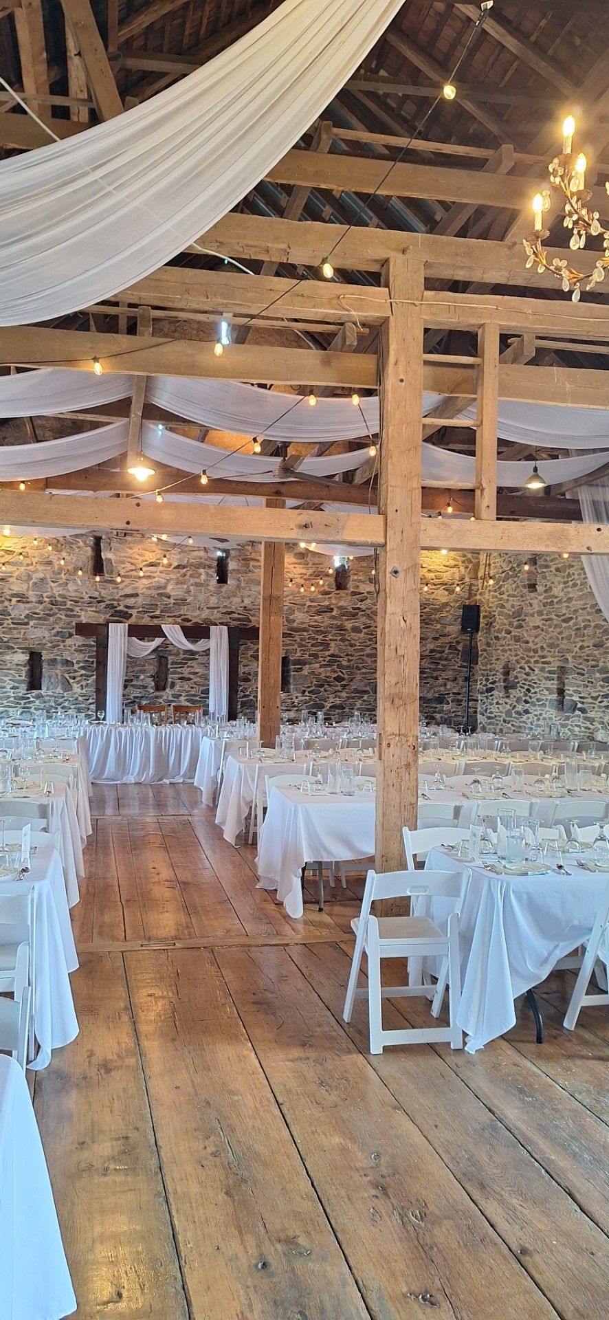 Wedding reception with white chairs, tables, and draped fabric under warm string lights