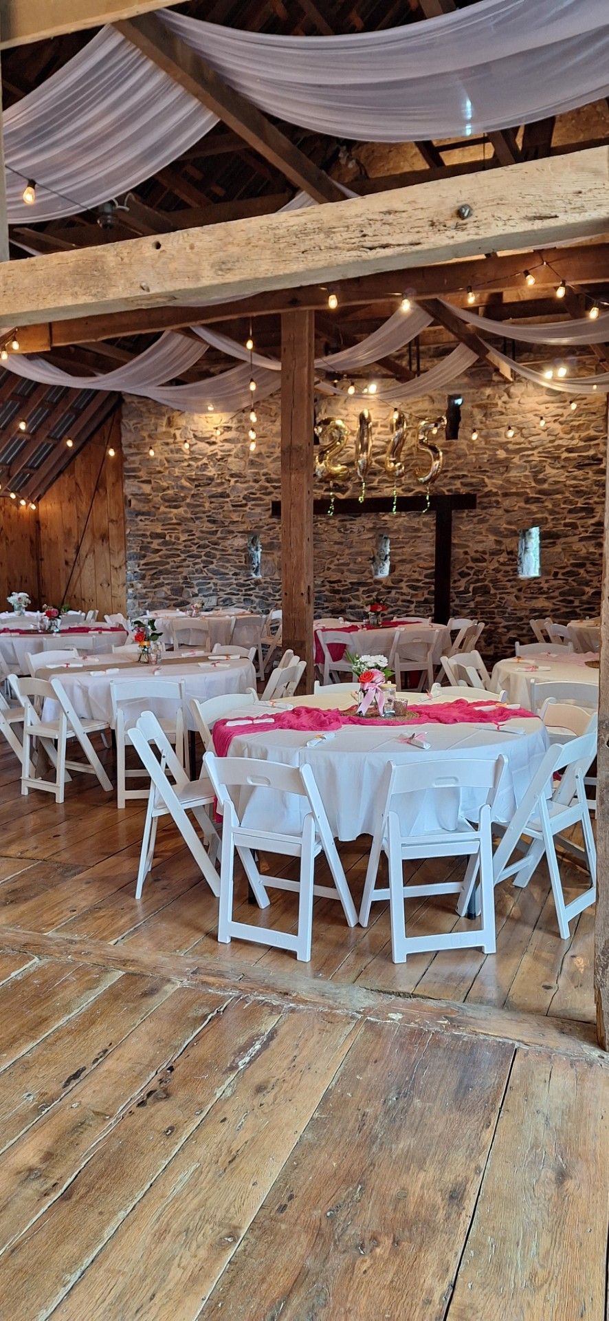 Banquet hall with white chairs, pink table settings, and draped ceiling decor