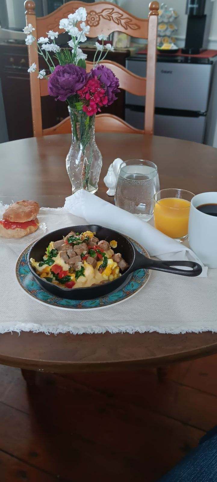 Breakfast on a table with a skillet of eggs and vegetables, orange juice, toast, and a vase of flowers