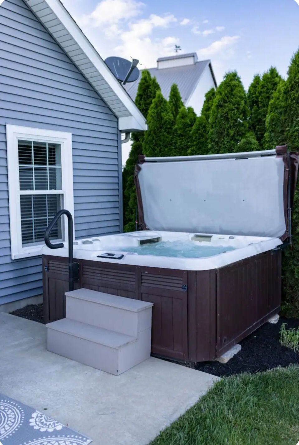 A hot tub is sitting outside of a house with the lid open.