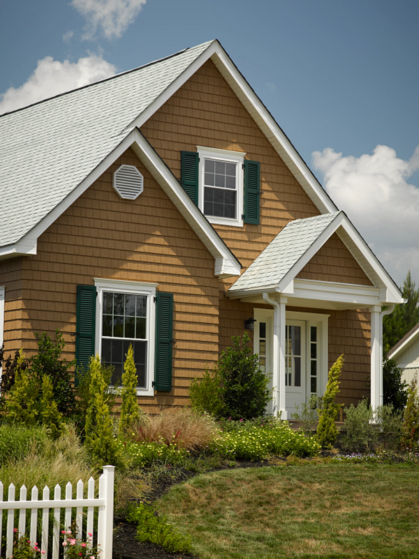 Small tan house with green shutters, white trim, and a front porch in a grassy yard under a blue sky