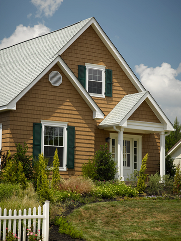 Small tan house with green shutters, white trim, and a front porch in a grassy yard under a blue sky