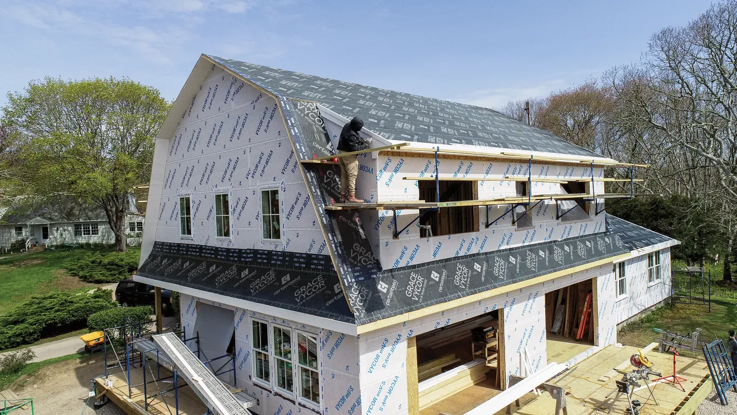 House under construction with workers on scaffolding and roof, white siding and black trim