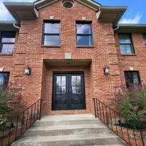 Brick townhouse entrance with black double doors, front steps, and iron railings