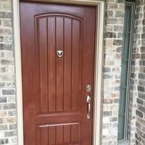 Front door with dark wood panels and silver handle set in a stone exterior wall.